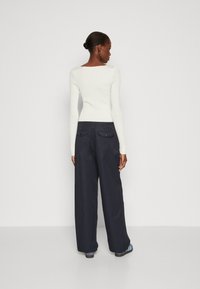 Un haut long à manches longues blanc côtelé associé à un pantalon large navy. Le pantalon possède des poches arrière avec des accents de bouton et une texture lisse.