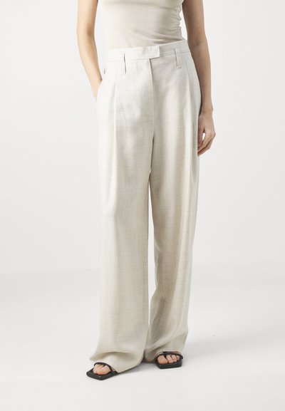 Φαρδιά παντελόνια από λινό σε μπεζ απόχρωση με υφή, διαθέτοντας δύο μπροστινές τσέπες και επίπεδη ζώνη. Φοριούνται με μαύρες σάνταλες.