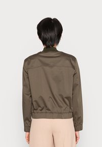 Giacca bomber color khaki con colletto a costine, polsini elastici e orlo. Tessuto liscio con dettagli di cuciture minime. Indossata da dietro.