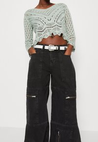 Mátově zelený háčkovaný crop top s ozdobným okrajem, v kombinaci s volnými černými cargo kalhotami, které mají několik kapes a zipů. Součástí je bílý pásek.