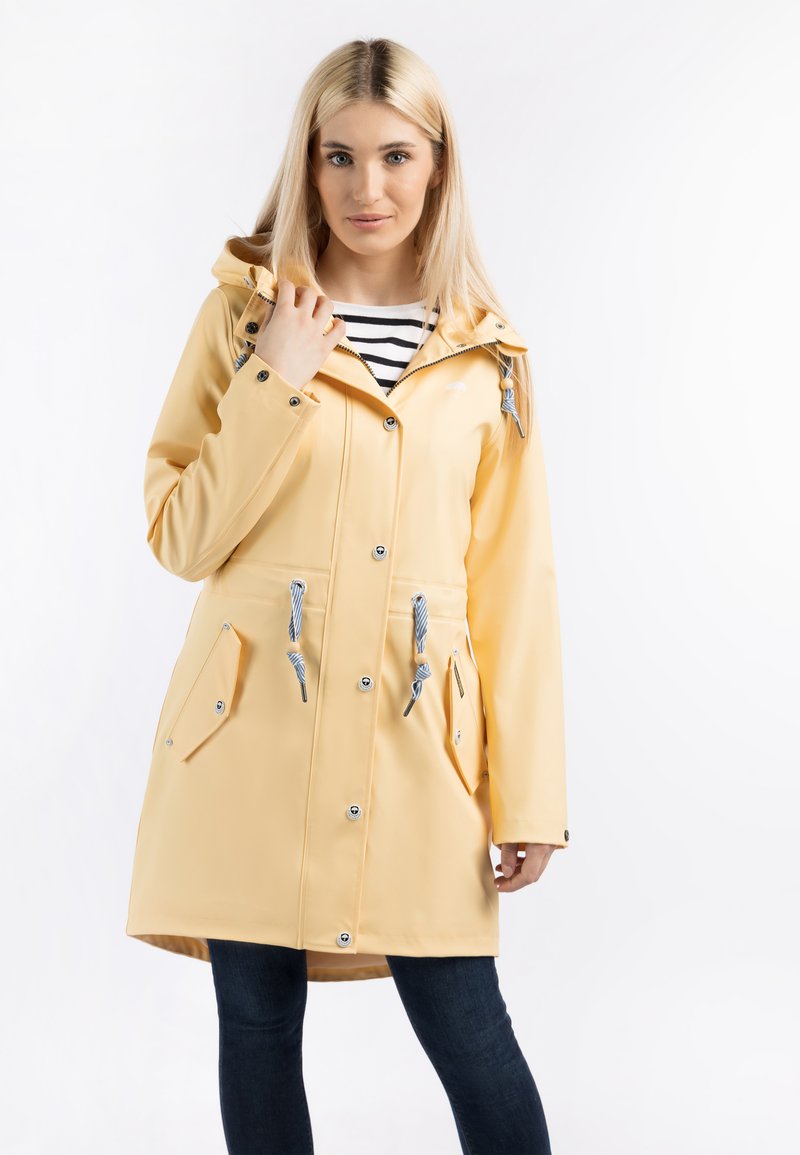 Chubasquero amarillo impermeable con capucha ajustable, botones a presión y dos bolsillos frontales. Presenta acentos de nudos en azul y blanco.