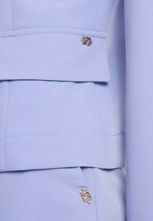 Abito azzurro chiaro su misura con ornamenti metallici dorati a forma di quadrato sul lembo della giacca e nell'area della tasca.