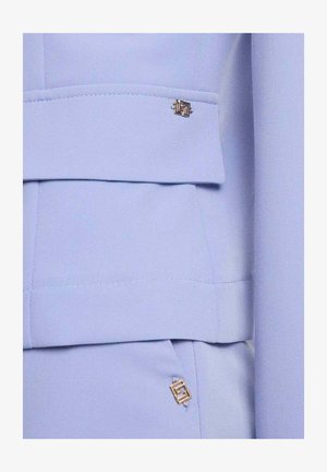 Abito azzurro chiaro su misura con ornamenti metallici dorati a forma di quadrato sul lembo della giacca e nell'area della tasca.