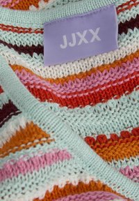 Textil de punto con rayas onduladas en azul claro, naranja, rosa y rojo profundo. Incluye una etiqueta púrpura con "JJXX". Hilo texturizado de múltiples colores.