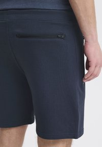 Marineblauwe shorts van zachte stof, met een ritszak op de achterkant, een aansluitende tailleband en een subtiele ribstructuur.