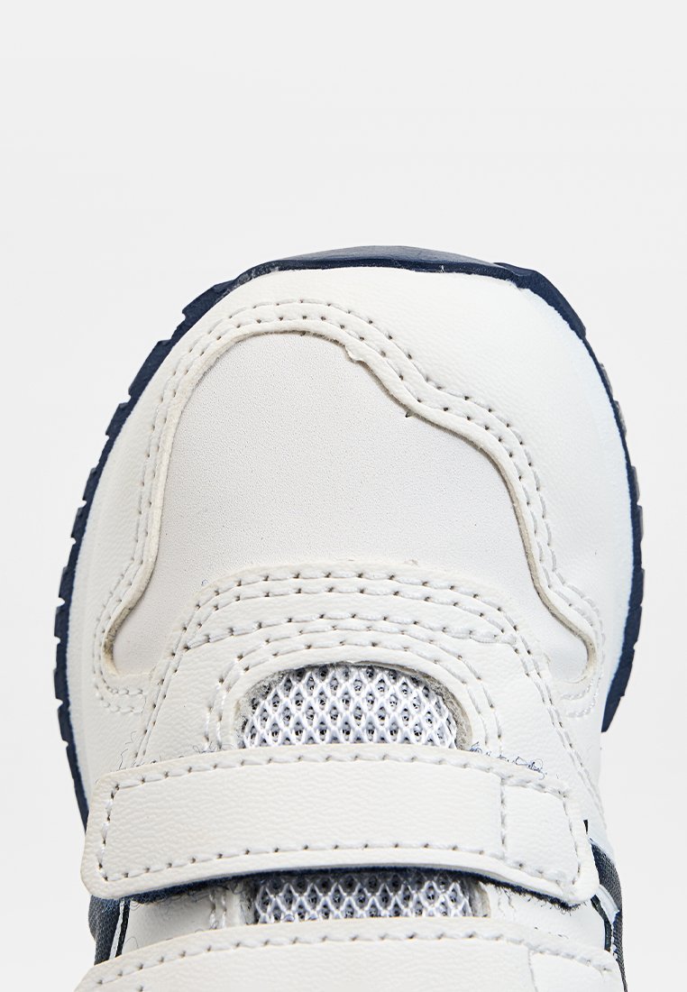 Baskets blanches avec accents bleu marine, présentant un bout rond, un panneau en maille et deux bandes Velcro. Matériau synthétique lisse avec des détails cousus.