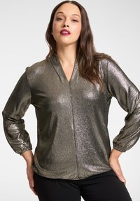 Blusa a maniche lunghe color oro scuro metallizzato con scollo a V, polsini elasticizzati e vestibilità morbida, realizzata in un tessuto scintillante.