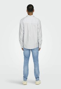 Witte en lichtblauwe gestreepte button-up shirt met een rugplooitje, gedragen met lichtblauwe jeans en beige sneakers.
