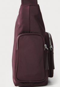 Borsa a tracolla in nylon marrone bordeaux con una texture liscia, una tasca frontale con zip e accessori in metallo argentato, caratterizzata da dettagli con nappine sulle cerniere.