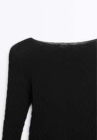 Black long-sleeve top made of textured knit fabric. Features a wide neckline and a subtle pattern throughout the material.