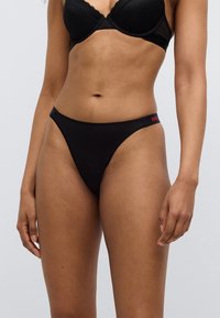 Μαύρο στρινγκ εσώρουχο με χαμηλή μέση, λεία υφή και κόκκινο λογότυπο στο λάστιχο της μέσης.