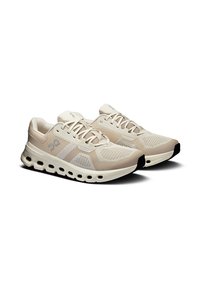 Beige színű futócipő pár, hálós felsőrésszel, fűzős kialakítással és párnázott talppal, hexagonális kivágásokkal a szellőzés érdekében.