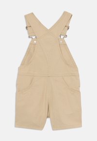 Salopette en coton beige avec bretelles ajustables, deux poches avant et détails de couture. Longueur short.