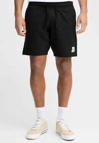 Pantaloni corti neri in cotone con vita elasticizzata, chiusura con cordoncino e un piccolo logo sul lato. Presentano una vestibilità comoda e una lunghezza fino a metà coscia.