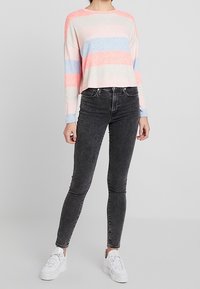 Svetr z bavlněného materiálu, zkrácený, s růžovými, modrými a bílými pruhy. V kombinaci s černými úzkými džíny a bílými teniskami.