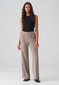 Tan wijde broek met verticale naden, gecombineerd met een strakke zwarte tanktop. De stof lijkt glad met een lichte glans.