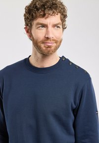 Sweatshirt bleu marine à col rond en tissu lisse, avec un col ribba et des boutons décoratifs sur l'épaule gauche.