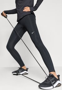 Black athletic leggings with contrast stitching and Nike logo, paired with black shoes featuring a white accent and a visible air unit.