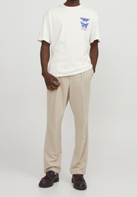 Bílá trička s grafikou motýla v modré a růžové barvě. Kombinováno se světle béžovými kalhotami a tmavými botami s texturovaným povrchem.