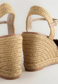 Wedge sandals with a braided natural jute heel, beige leather strap, and a smooth light brown insole. Textured, open-back design.