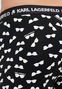 Boxer neri con un motivo ripetuto di occhiali da sole bianchi. L'elastico presenta il nome "KARL LAGERFELD" in lettere nere.