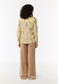 Lightweight, patterned blouse with yellow, brown, and cream hues; features long sleeves and a relaxed fit, paired with beige wide-leg trousers.