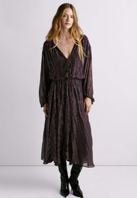 Vestido morado de longitud media con diseño de rayas verticales en varios colores. Cuenta con un escote en V profundo, cierre de botones y cintura recogida. Mangas largas.