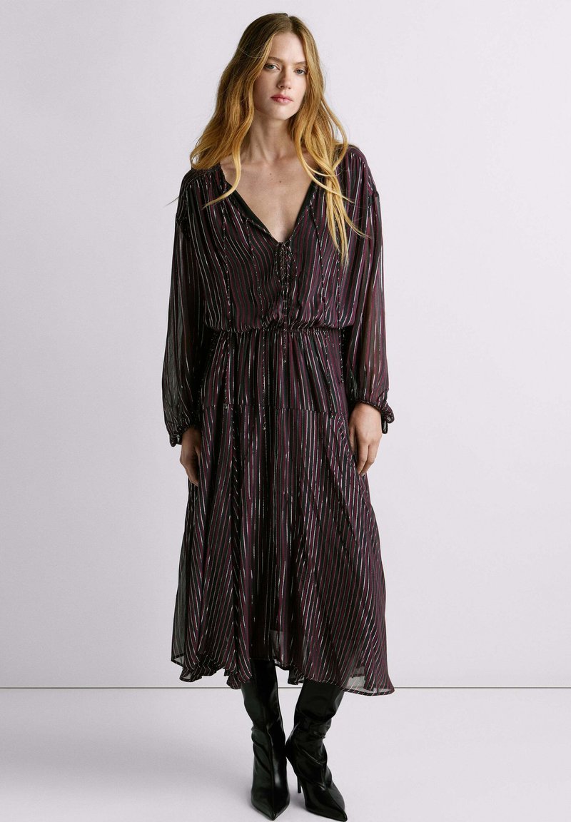 Vestido morado de longitud media con diseño de rayas verticales en varios colores. Cuenta con un escote en V profundo, cierre de botones y cintura recogida. Mangas largas.