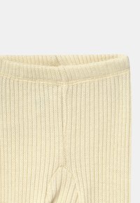 Leggings côtelés couleur crème avec une texture douce et une taille élastique, présentants une forme légèrement arrondie au niveau des genoux.