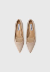 Μπεζ γόβες με μυτερή μύτη, επάνω μέρος από λείο ύφασμα, ανατομική σόλα και μίνιμαλ σχεδιασμό. Φέρουν λογότυπο στα πέλματα.