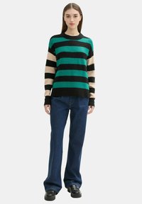 Gestreifter Pullover mit smaragdgrünen, schwarzen und beigen horizontalen Streifen; lockere Passform; Woll-Mischmaterial; kombiniert mit weiten Jeans und klobigen Schuhen.