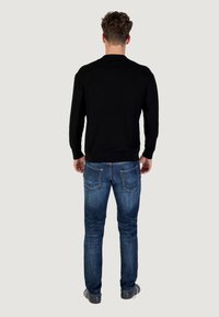 Cardigan nero a maglia con colletto rotondo, schiena texture, abbinato a jeans in denim blu con cuciture in contrasto e vestibilità slim.