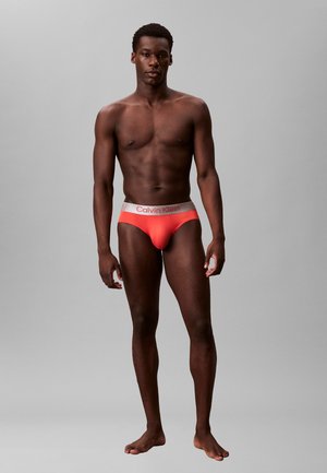 Męskie slipy Calvin Klein w jasnym koralowym kolorze z kontrastującym szarym pasem, na którym znajduje się logo. Miękki, elastyczny materiał zapewniający dopasowanie.