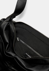 Sort læderhandtaske med en blød tekstur, lynlåslukket hovedrum og indvendig lomme, der har et mærket branding-tag indeni.