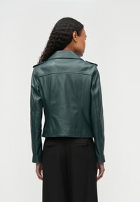 Temno zelena usnjena jakna s kratkim krojem, širokim ovratnikom in ramenskimi naramnicami. Gladek tekstura z vidnimi šivi.