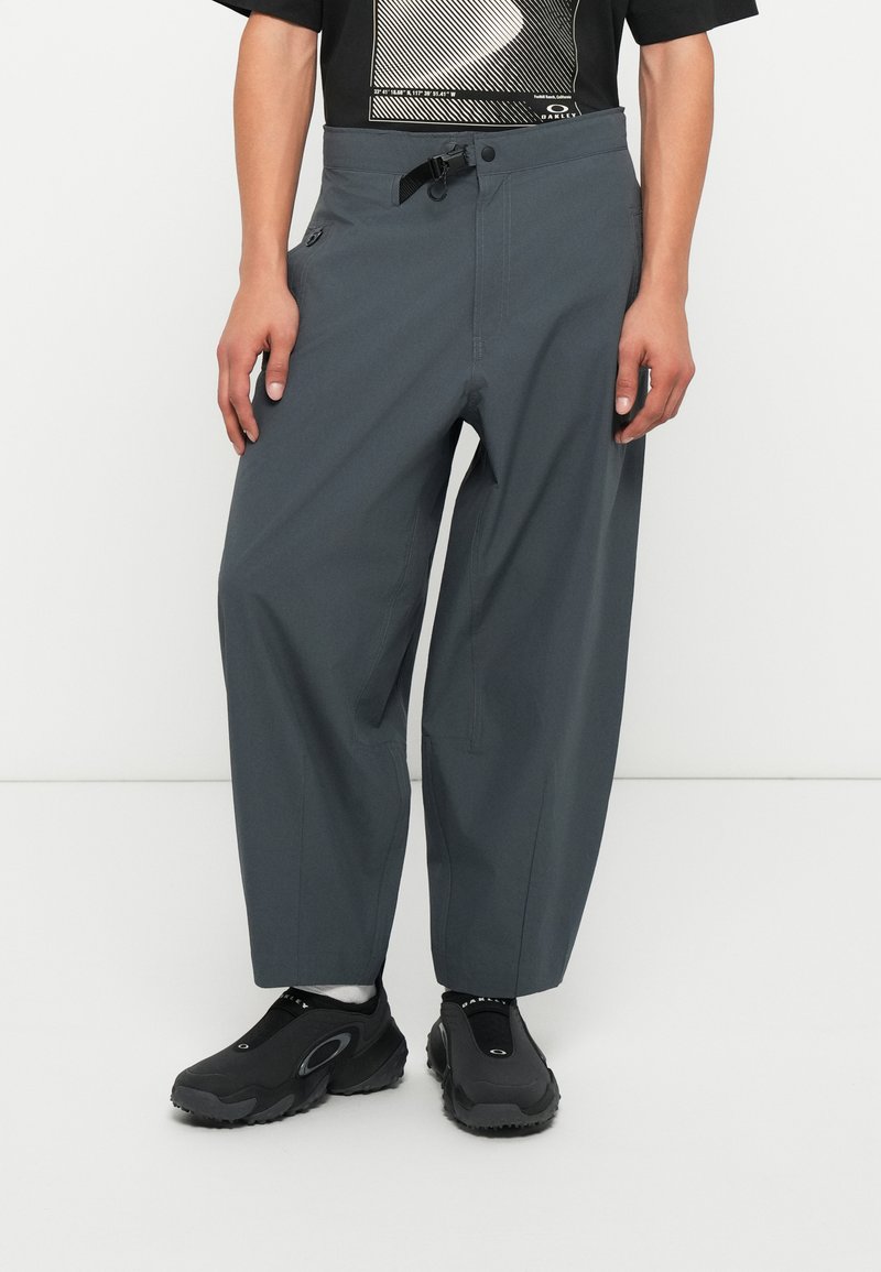 Pantaloni grigi larghi con vita regolabile, dotati di tasche laterali e in tessuto morbido. Abbinati a sneaker nere senza lacci.