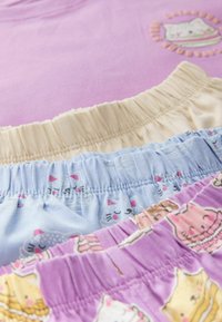 Vier paar kleurrijke kinderonderbroeken: beige, lichtblauw met kattenpatronen en roze met dessert-thema prints. Zacht stof en elastische taillebanden.