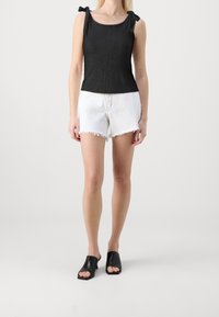 Haut noir sans manches avec bretelles à nouer, tissu texturé ; short blanc taille haute avec ourlet effiloché ; mules à talons ouvertes noires.
