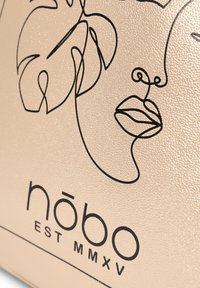 Gouden textuur met zwart lijntekeningontwerp van een gezicht en bladeren. Bevat de merknaam 'nōbo' en 'EST MMXV' in vette letters.