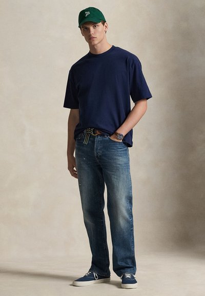 Μπλε βαμβακερό μπλουζάκι ναυτικού τύπου, ανοιχτό μπλε τζιν, πράσινο καπέλο, casual αθλητικά παπούτσια; ορατό ρολόι, μινιμαλιστικός σχεδιασμός, άνετη εφαρμογή, διακριτικές φθορές στο τζιν.