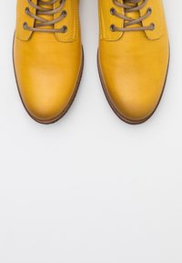 Żółte skórzane buty z okrągłymi noskami, teksturowanym wierzchem i brązowymi sznurówkami, posiadające wzmocnione oczka oraz kontrastujące ciemnobrązowe podeszwy.
