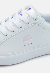 Baltas odinis sportbačių modelis su apvaliais raišteliais, rožiniu krokodilo logotipu ir struktūrizuota padu. Papuoštas blizgančia liežuvėlio etikete.