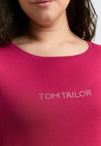 Fuchsia T-Shirt mit Rundhalsausschnitt, glatter Textur und dem Markennamen "TOM TAILOR", der mit Strasssteinen verziert ist.