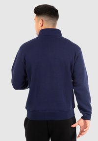 Felpa navy con collo alto, maniche lunghe, polsini e orlo ribattuti. Texture liscia, design minimalista, adatta per un look casual.