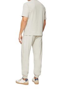 Lichtgrijs, zacht stoffen outfit bestaande uit een kortmouwtop en smal toelopende sweatpants, gecombineerd met witte en marineblauwe sneakers.