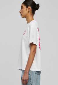 Hvit t-skjorte med korte ermer og rosa grafisk trykk foran og bak. Løs passform med rund hals og myk tekstur.