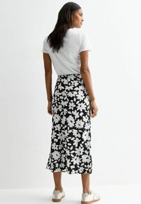 Jupe maxi florale noir et blanc avec un ourlet évasé, assortie à un t-shirt blanc uni et des baskets de couleur claire. Texture de tissu douce.