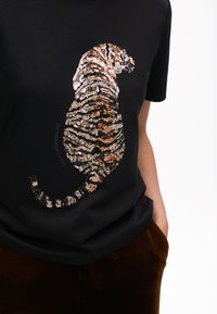 T-shirt nera con design di tigre in paillettes oro, bronzo e argento, con una vestibilità leggermente larga e maniche corte.