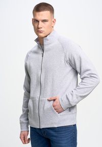 Szara bluza z suwakiem, z wysokim kołnierzem, kieszeniami z przodu i ściągaczami; charakteryzuje się miękkim materiałem i luźnym krojem.