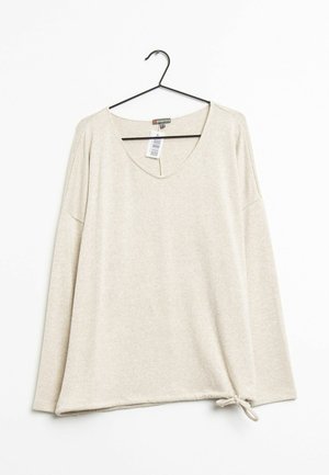 Beiger Langarmpullover mit V-Ausschnitt, an einem schwarzen Bügel hängend, mit seitlicher Bindung am Saum.